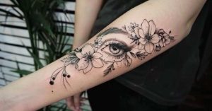 Tatuagem feminina no braço com olho e flores em estilo fino e detalhado.