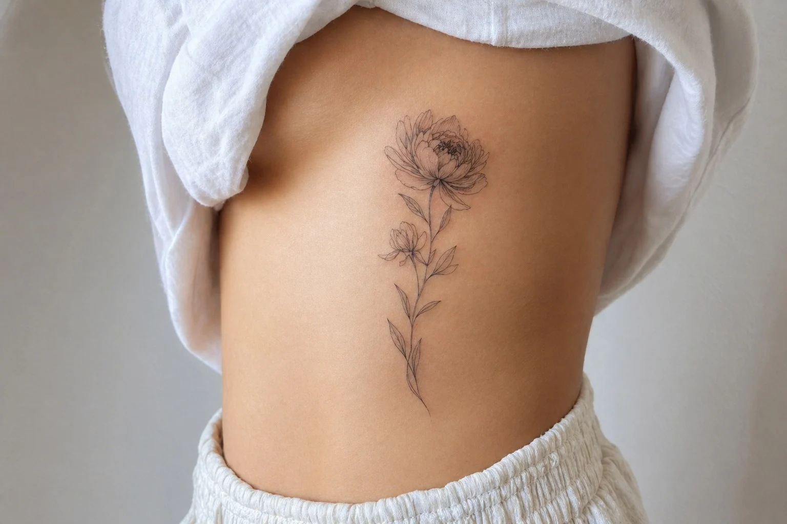 Tatuagem feminina de peonia na costela com desenho vertical delicado