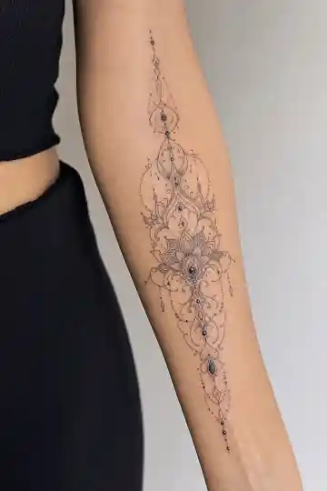 Tatuagem ornamental feminina no antebraço com mandala alongada e detalhes de joia