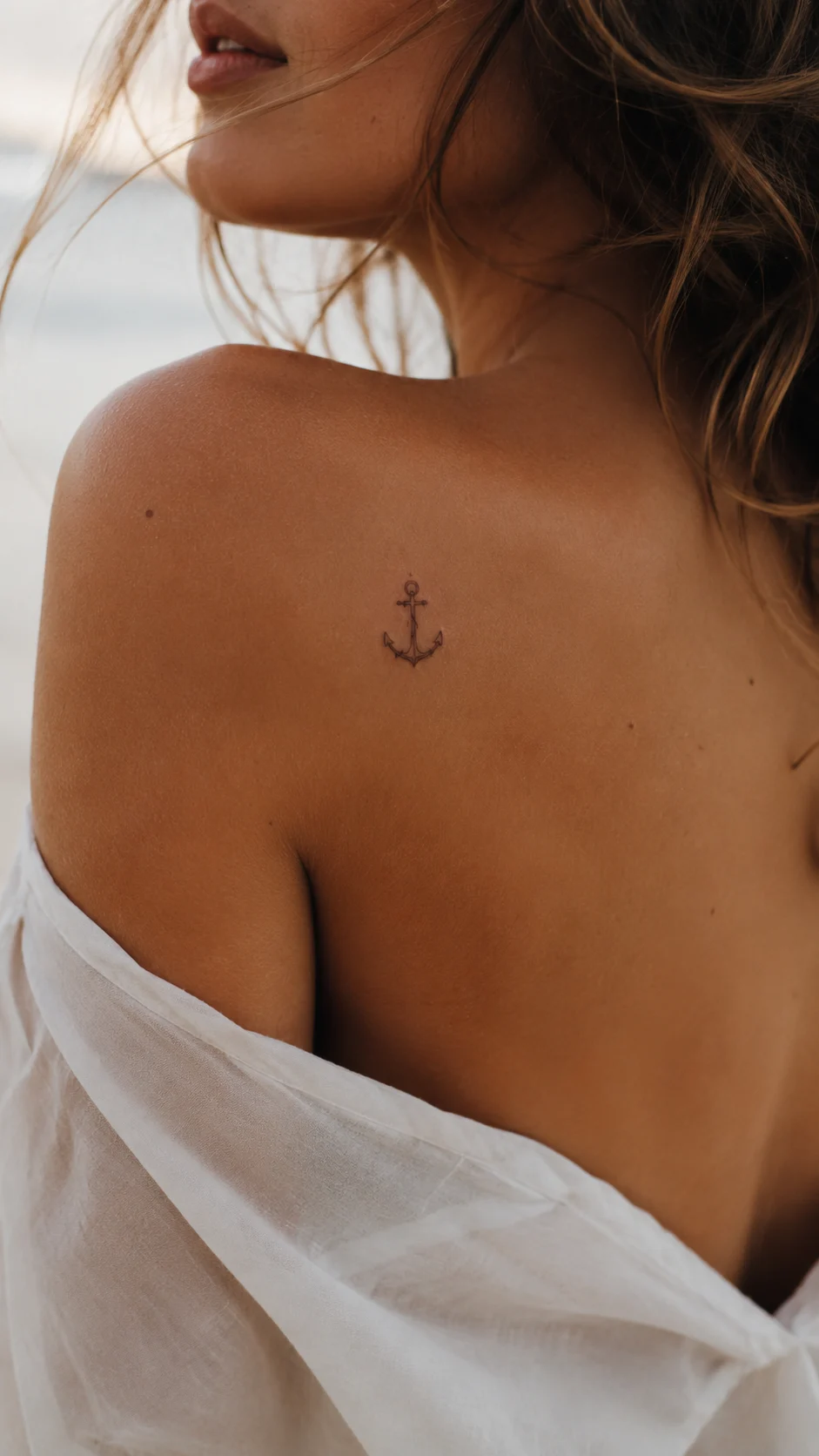 Pulso com uma pequena tatuagem de âncora em traço fino.
