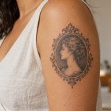 Referência gerada com IA de tatuagem de camafeu ornamental em preto e cinza no braço feminino