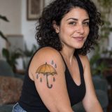 Guarda-chuva amarelo com gotas tatuado no braço de mulher adulta