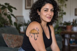 Guarda-chuva amarelo com gotas tatuado no braço de mulher adulta