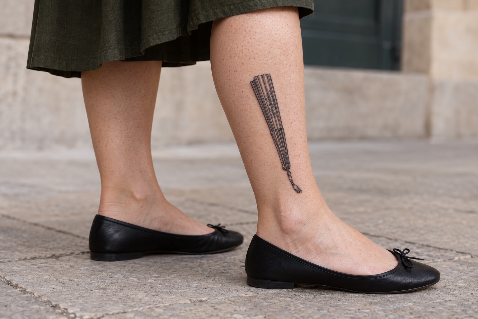 Leque fechado com cordão curto tatuado na panturrilha de mulher adulta